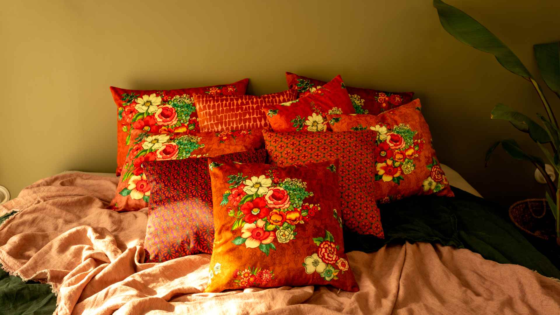 une serie de coussins velours aux touches de couleurs ocre et rose sur un lit