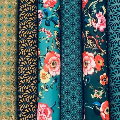 Rollos de telas Vent de bohème con motivos florales y gráficos en azul petróleo, coral y dorado